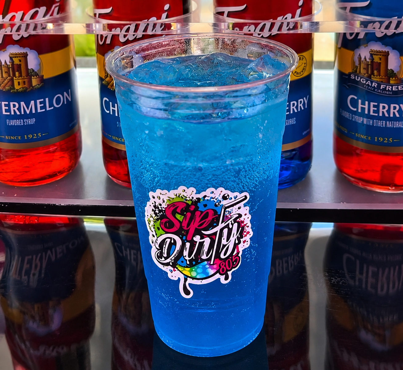 Blue PCH Punch dirty soda in a Sip Dirty 805 cup with Torani syrups behind it